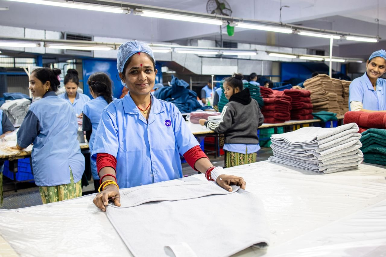 services-01 Smiling Indian factory workers in textile industry folding fabrics indoors.