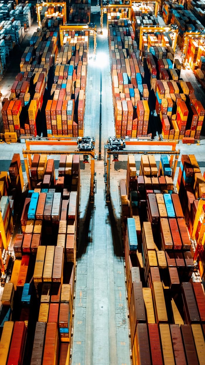 Services Aerial view of organized cargo containers in a brightly lit warehouse at night.