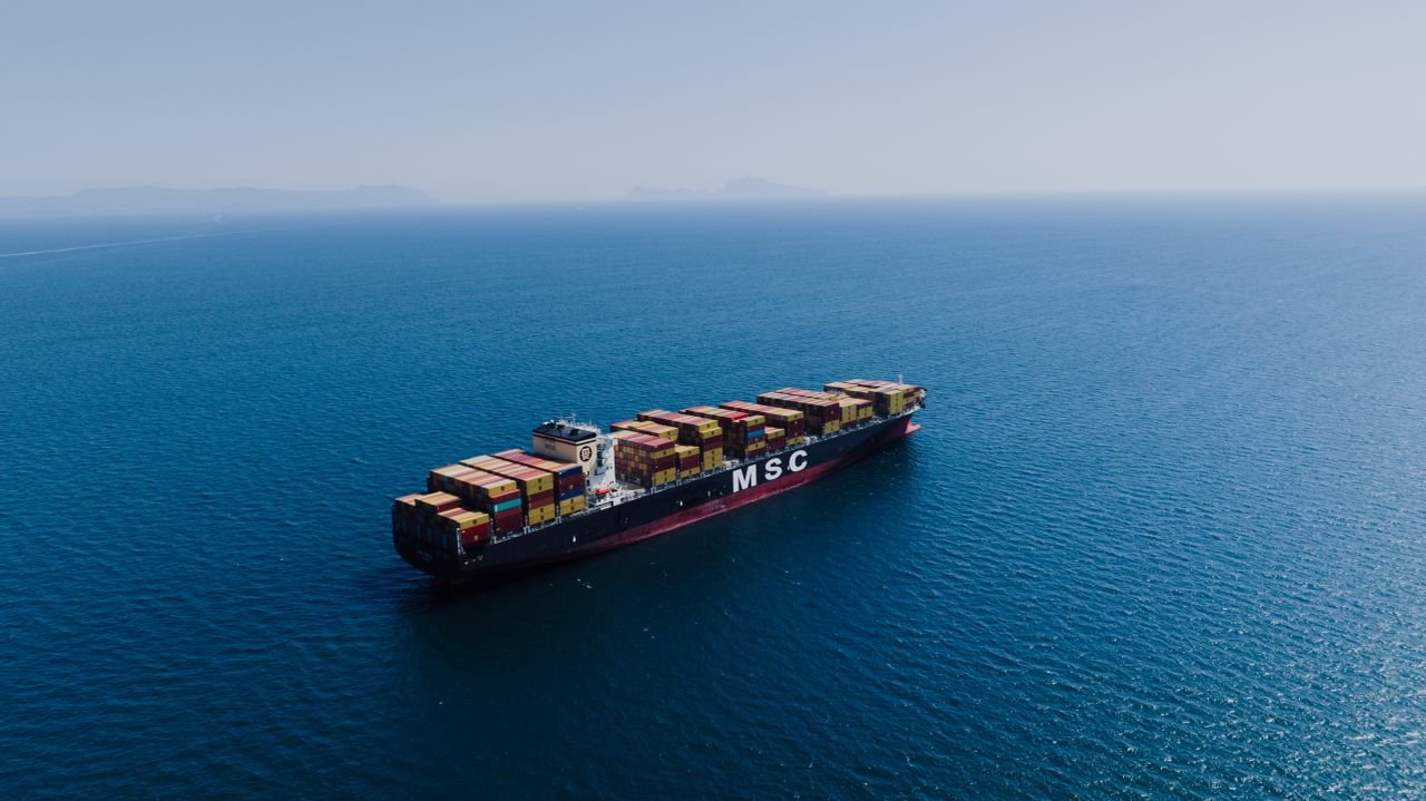 Services An aerial shot of a loaded container ship sailing near Naples, Italy under clear blue skies.