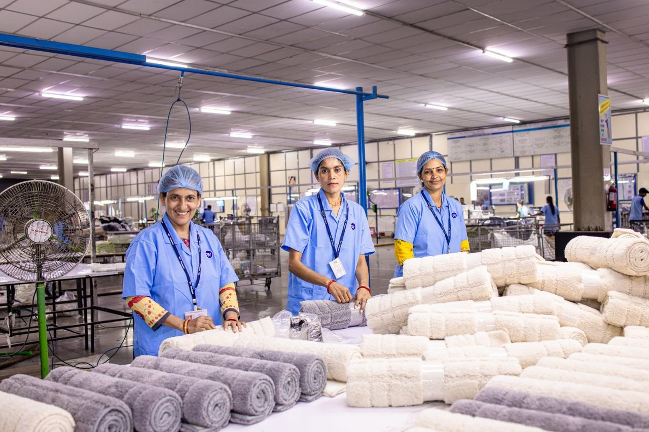 Three female workers in blue uniforms rolling towels in a textile factory.