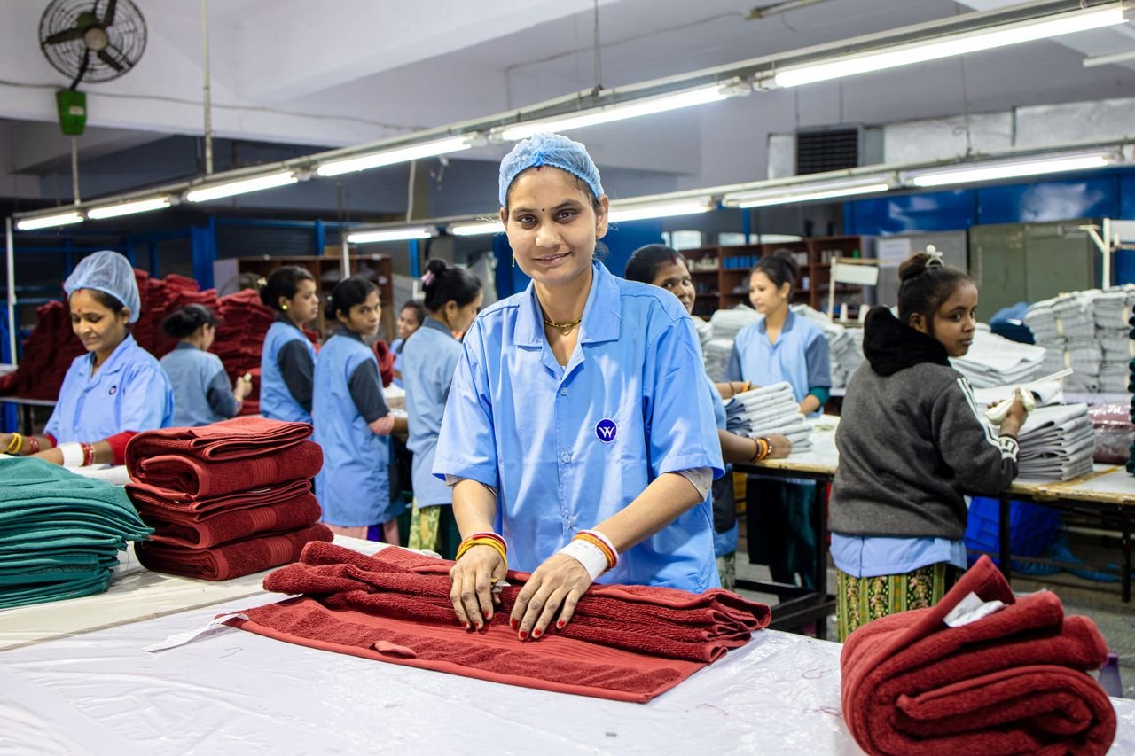 Textile factory workers in blue uniforms folding red and green fabrics indoors.
