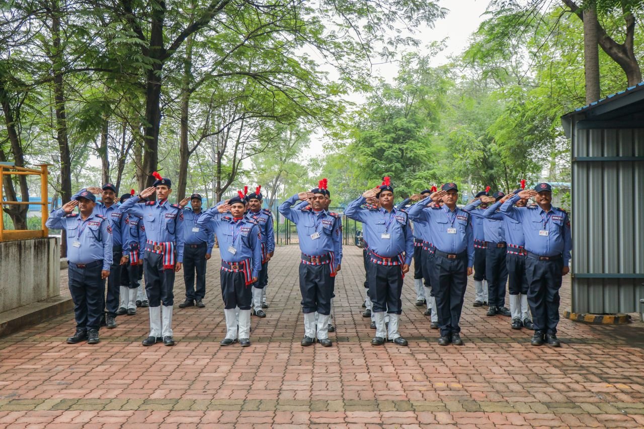 Uniformed guards in an outdoor setting performing a salute. Orderly formation under trees.