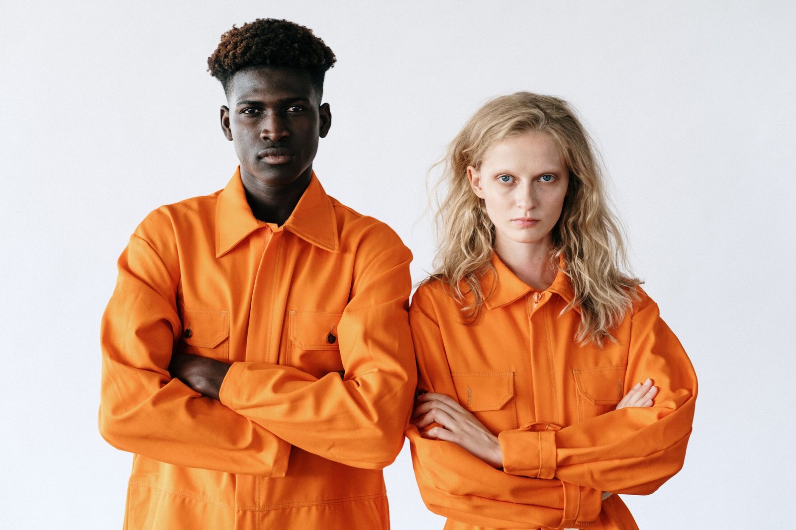Portrait of a diverse pair in vibrant orange work uniforms with determined expressions.