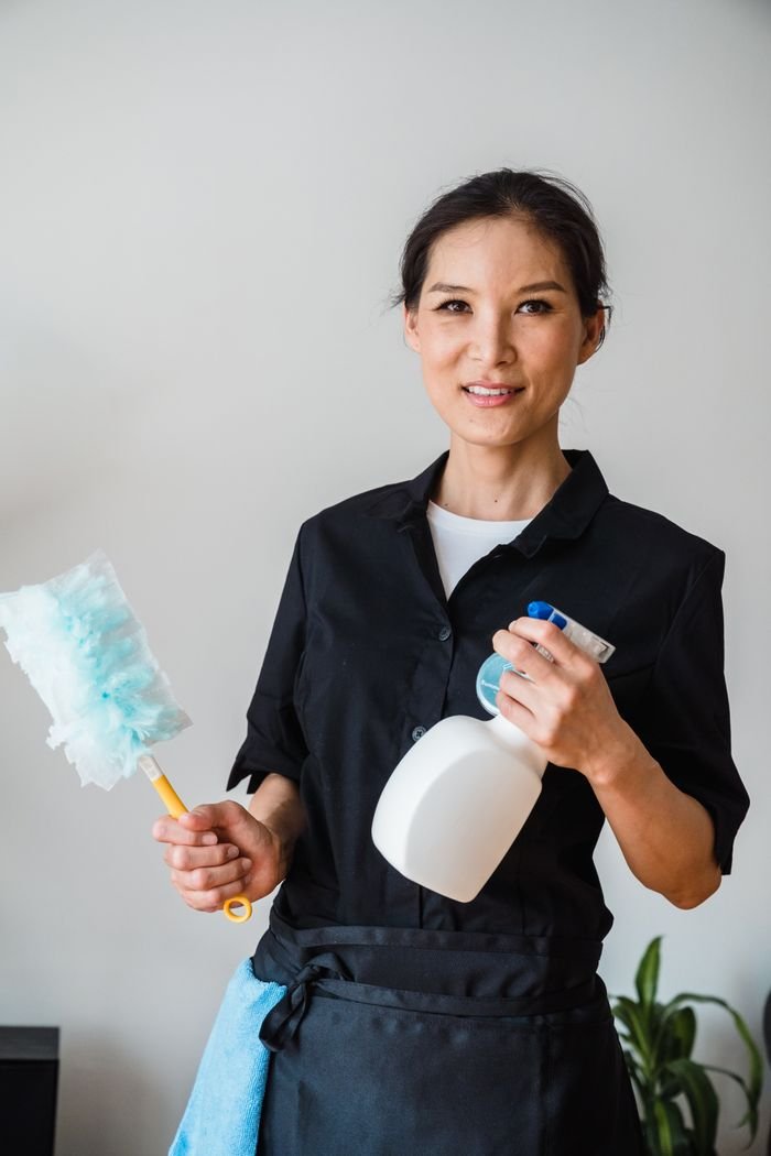 A female housekeeper smiling while holding cleaning tools indoor.