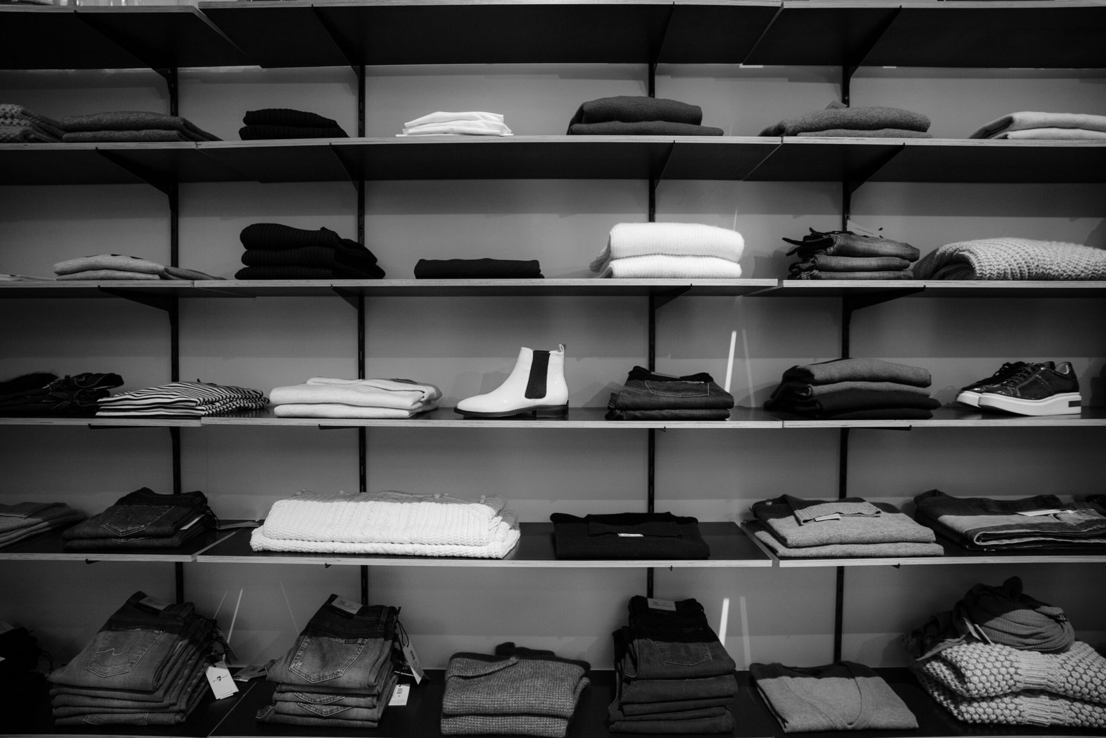 Home Neatly folded clothing and shoes displayed on shelves in a boutique setting.