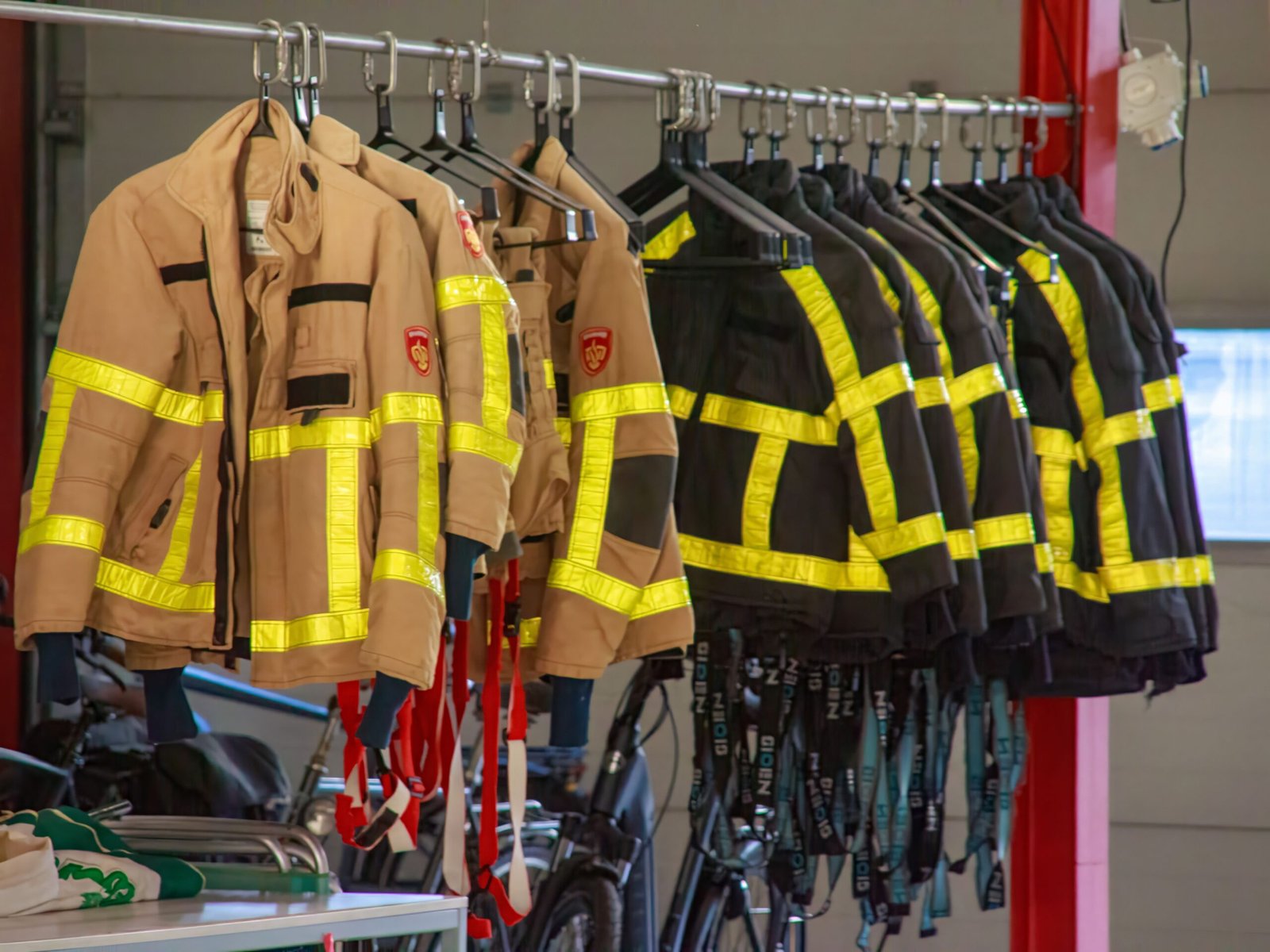 Home Firefighter uniforms with reflective strips hanging in a garage setting.