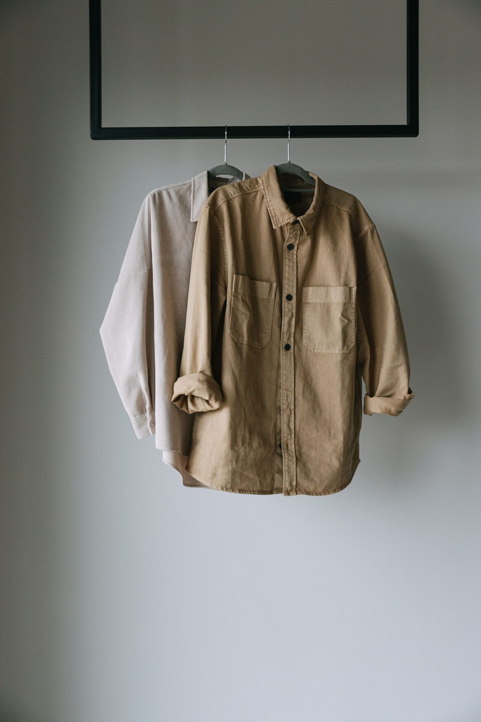Home Two neutral shirts hanging on a rack, perfect for minimalist fashion concepts.